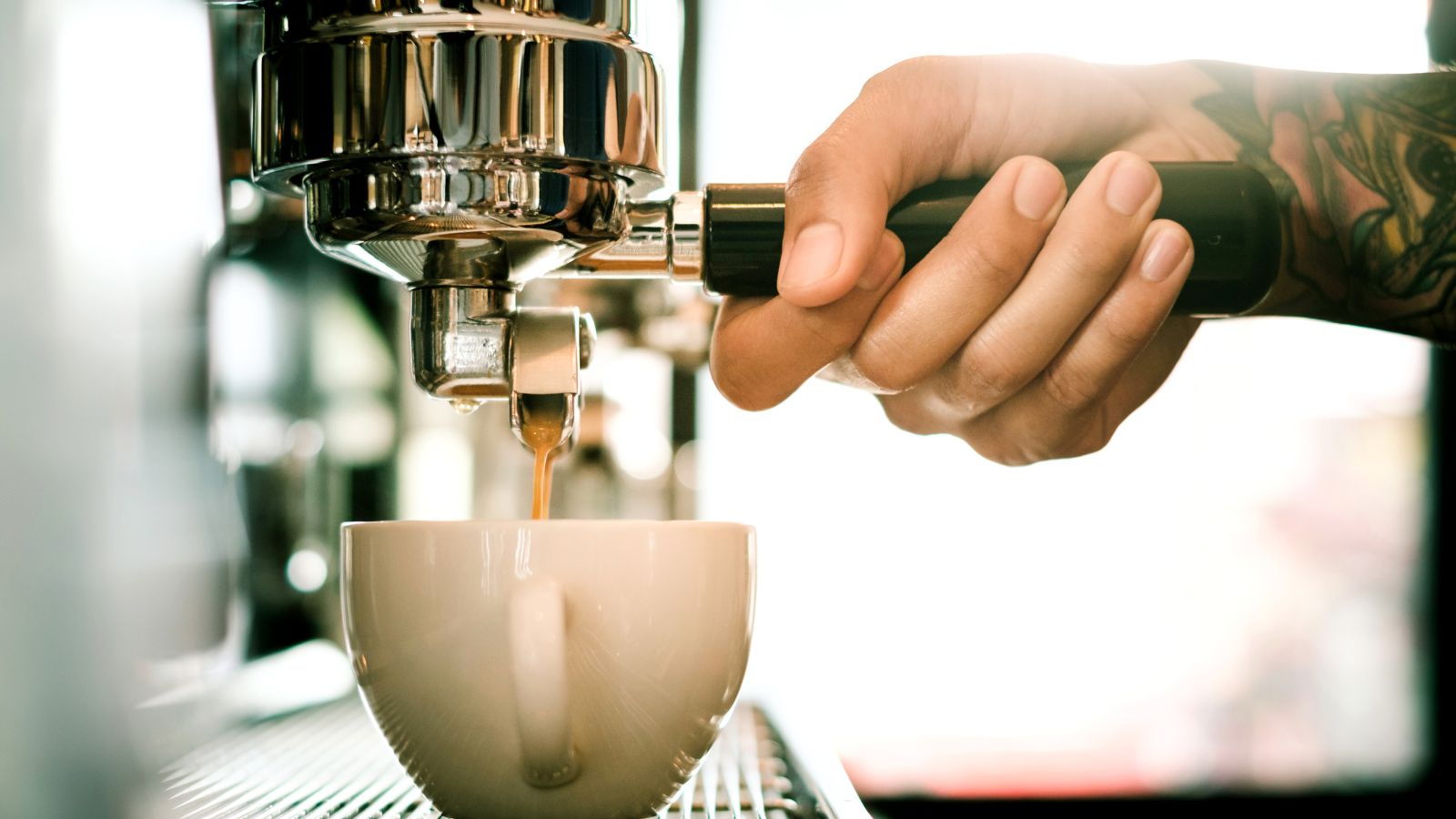 Barista pulling espresso into a cup with tattooed hand