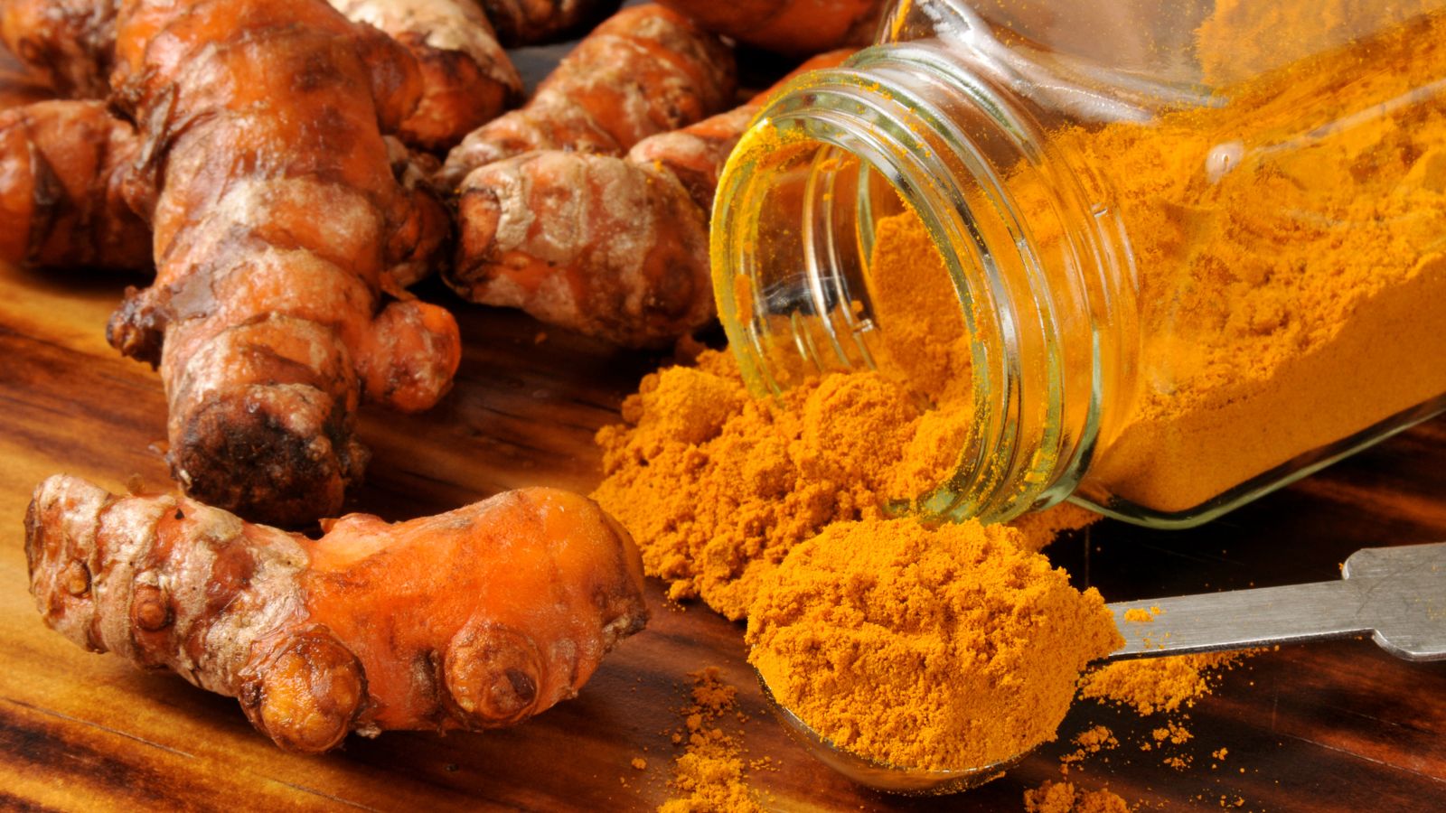 Turmeric roots and powder spilling from jar onto wooden surface