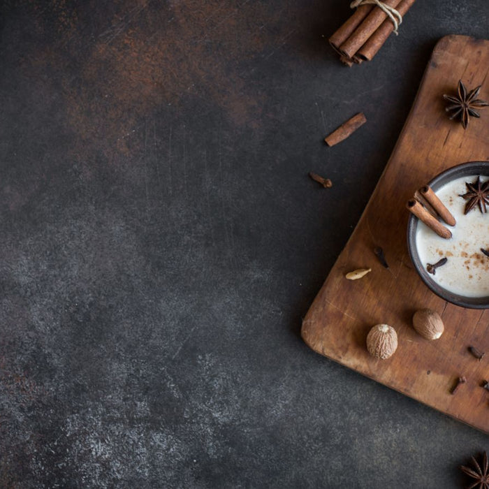 Warm chai tea in dark mug with star anise and spices on wooden board.