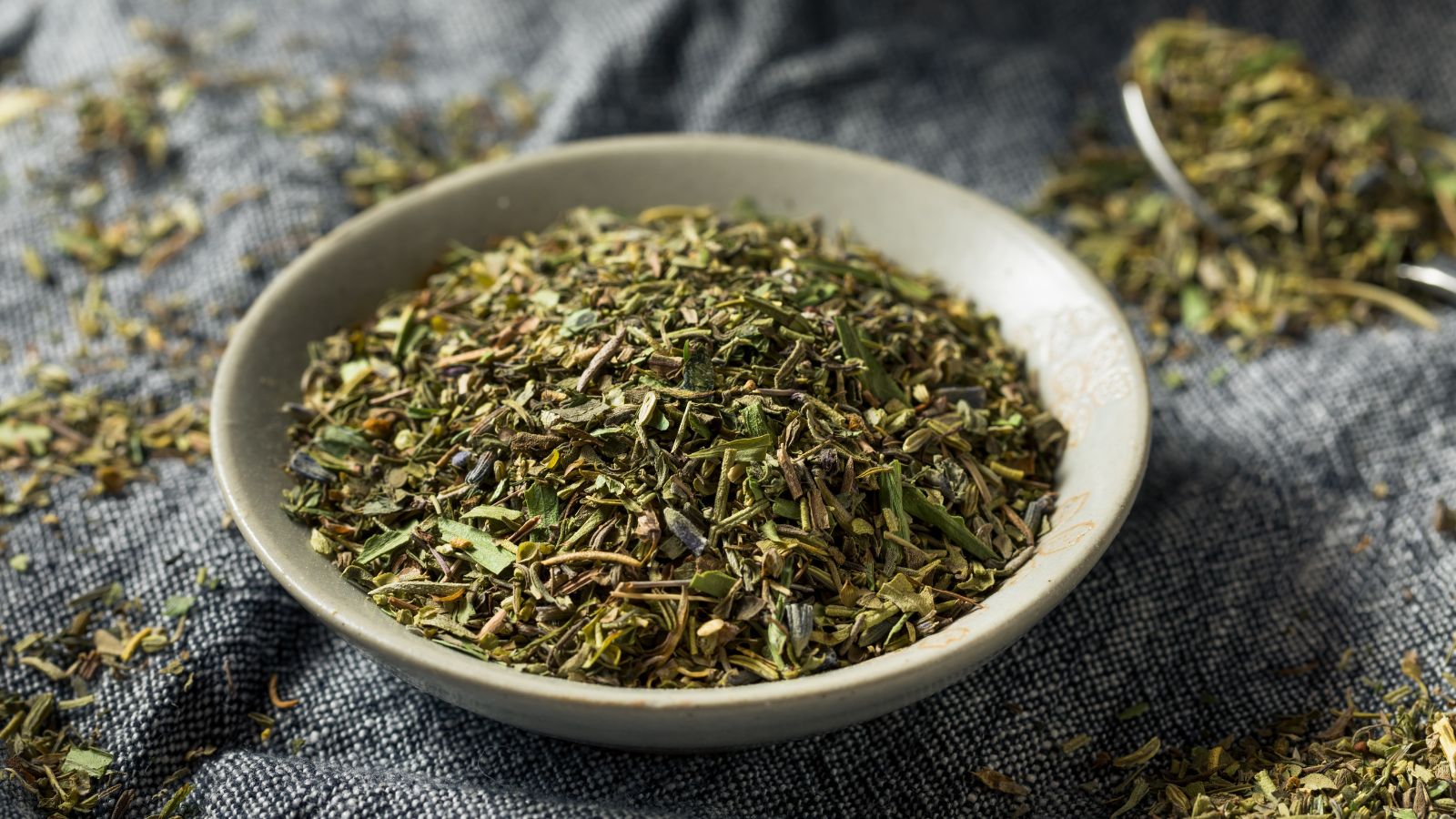 Herbs de Provence in a ceramic bowl on a gray cloth surface.