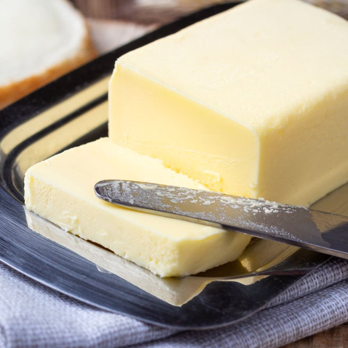 Butter curl on a knife beside a block of butter on a tray.