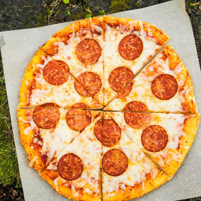 Pepperoni pizza on parchment paper atop tree stump outdoors.