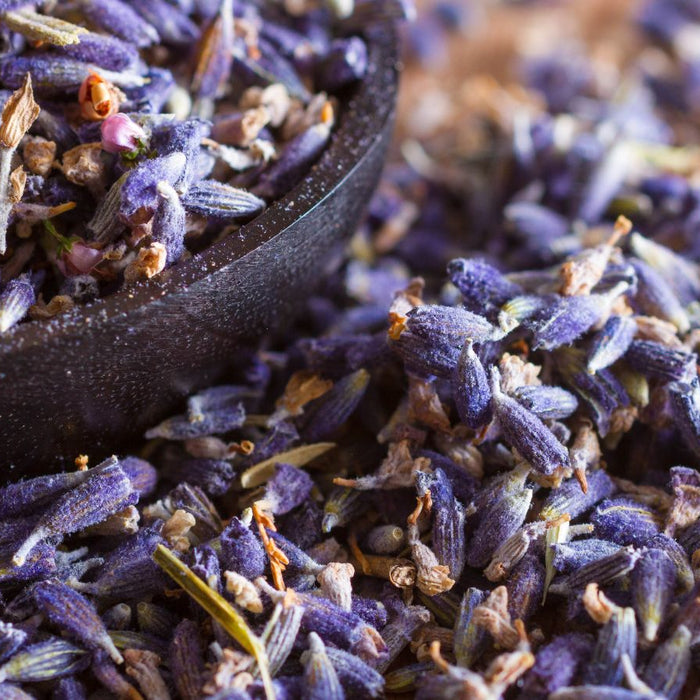 Stone cottage among purple lavender rows under sunset mountain sky.