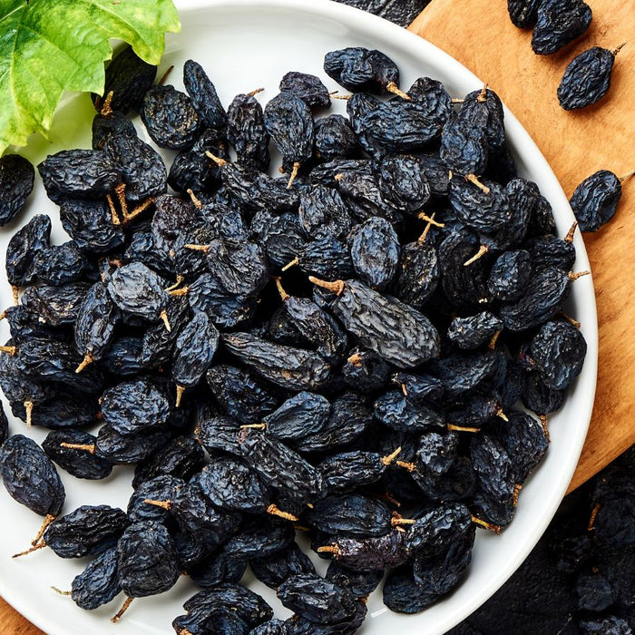 White plate filled with black raisins placed on a wooden board.