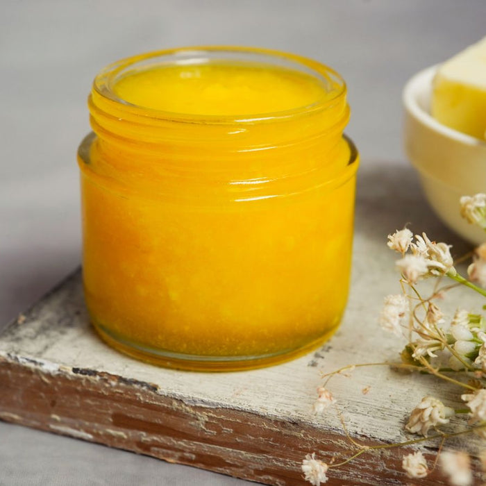 Glass jar of ghee with butter cubes and dried flowers.