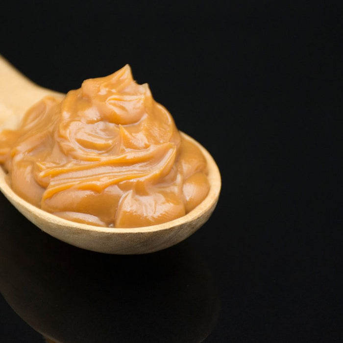 Wooden spoon with a swirl of smooth caramel on black background.