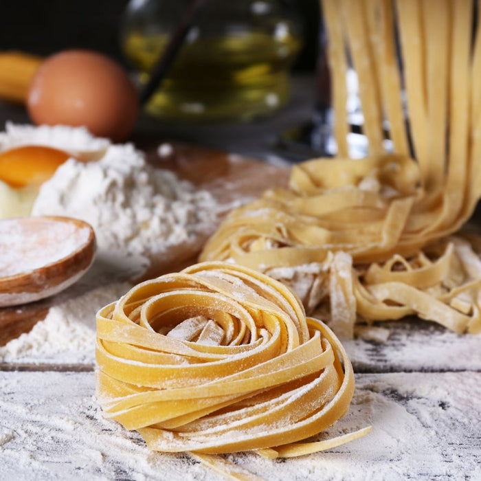 Fresh homemade fettuccine pasta being rolled and shaped with flour