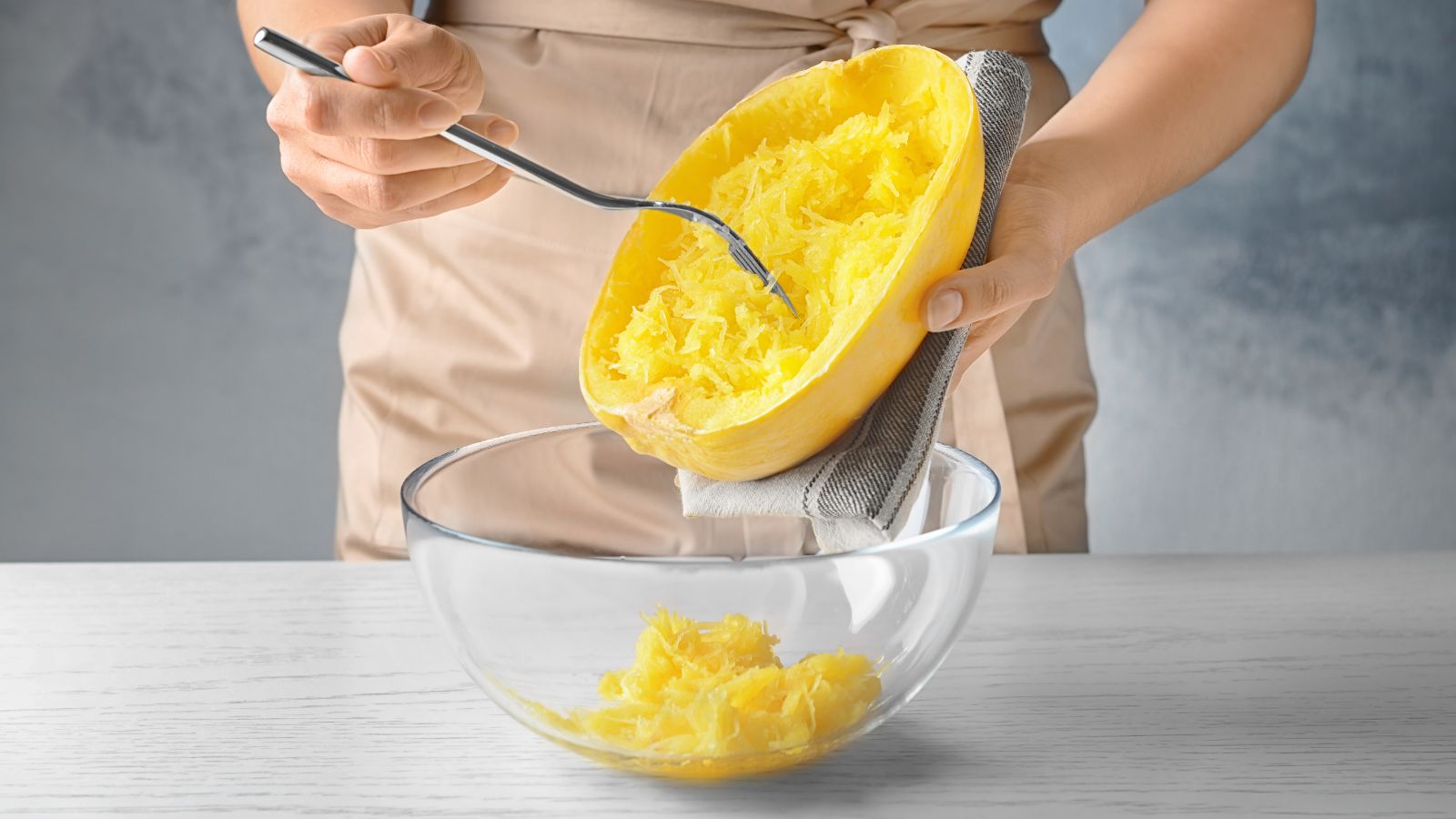 Person scraping cooked spaghetti squash into glass bowl