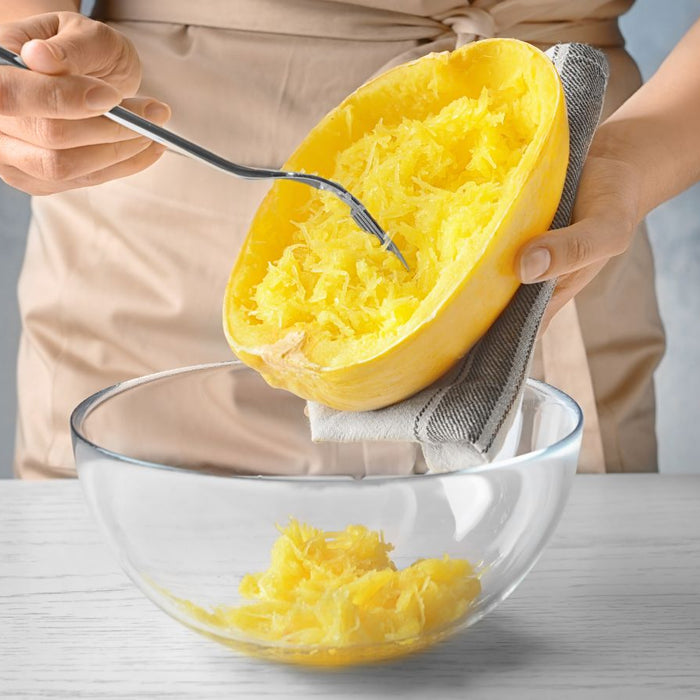 Person scraping cooked spaghetti squash into glass bowl