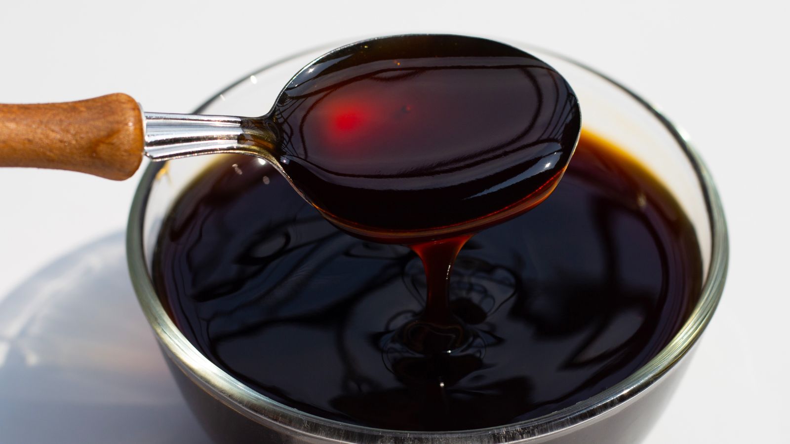 Spoon dripping thick dark oyster sauce into a glass bowl on a table