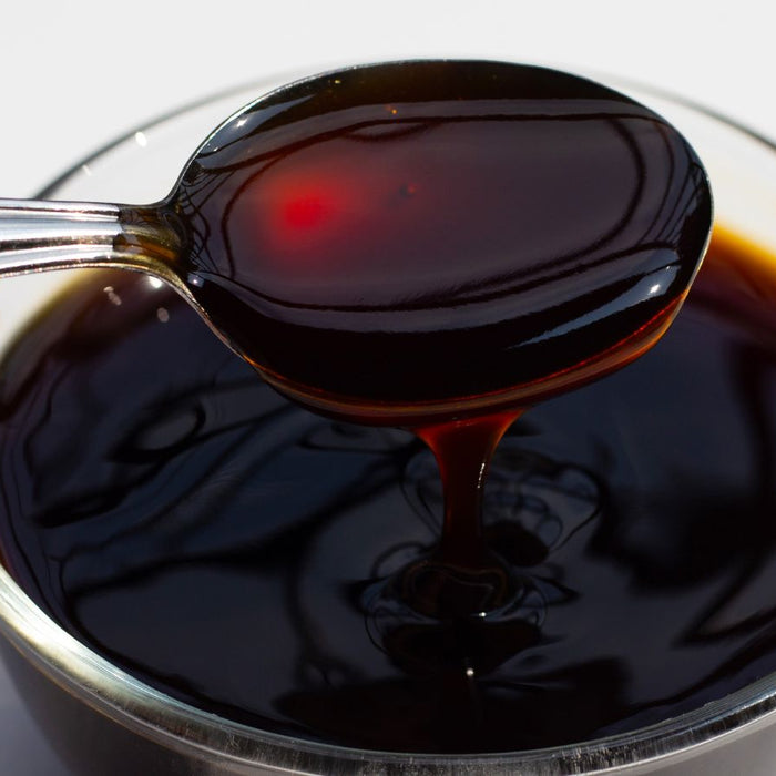 Spoon dripping thick dark oyster sauce into a glass bowl on a table