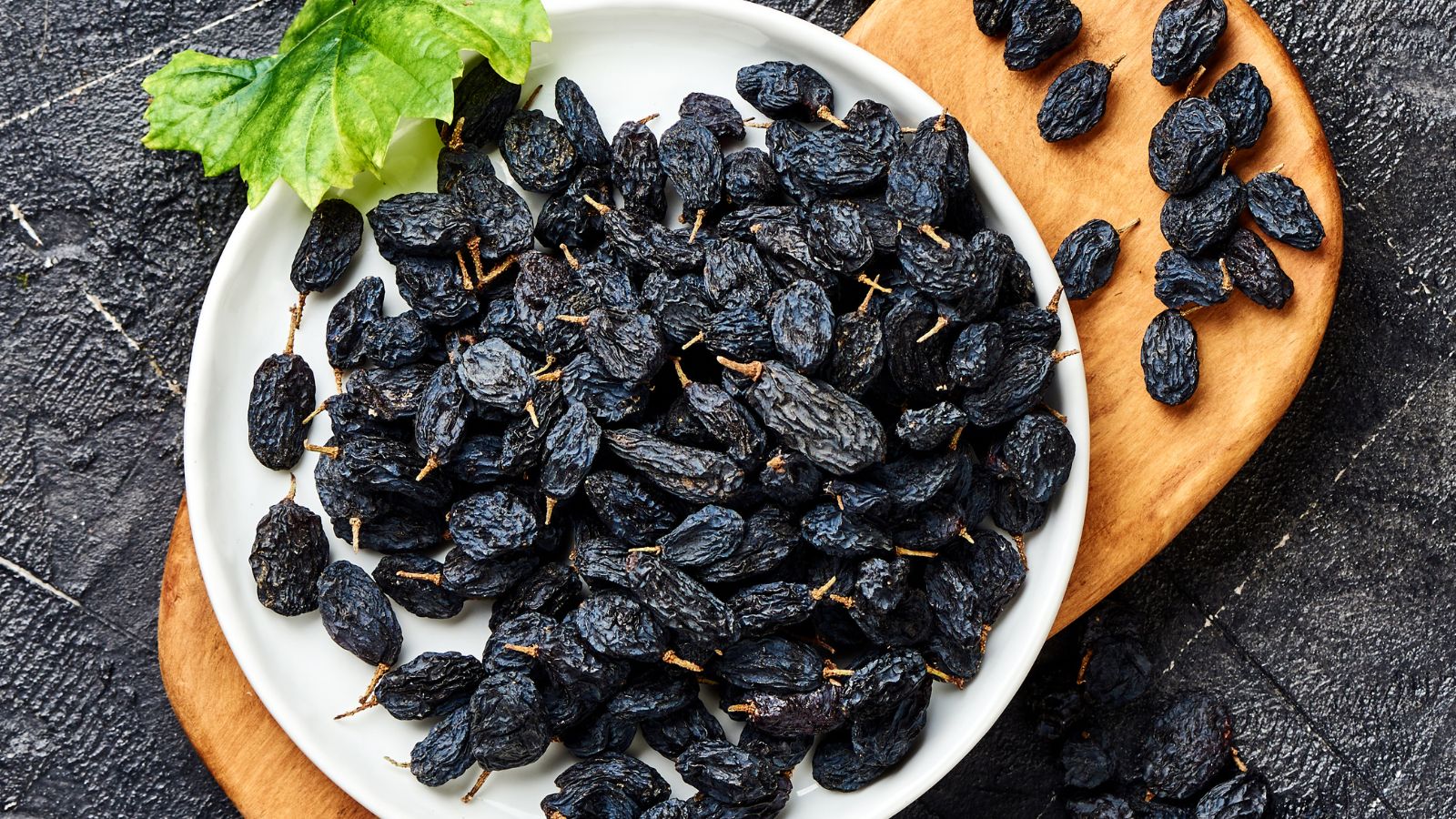 White plate filled with black raisins placed on a wooden board.
