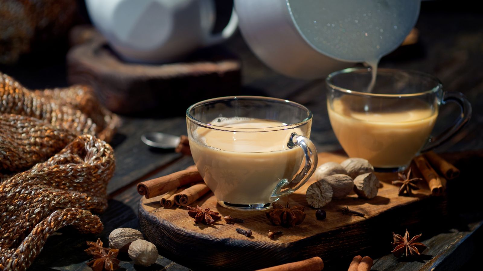 Two glass cups of chai tea with spices and a cozy setting
