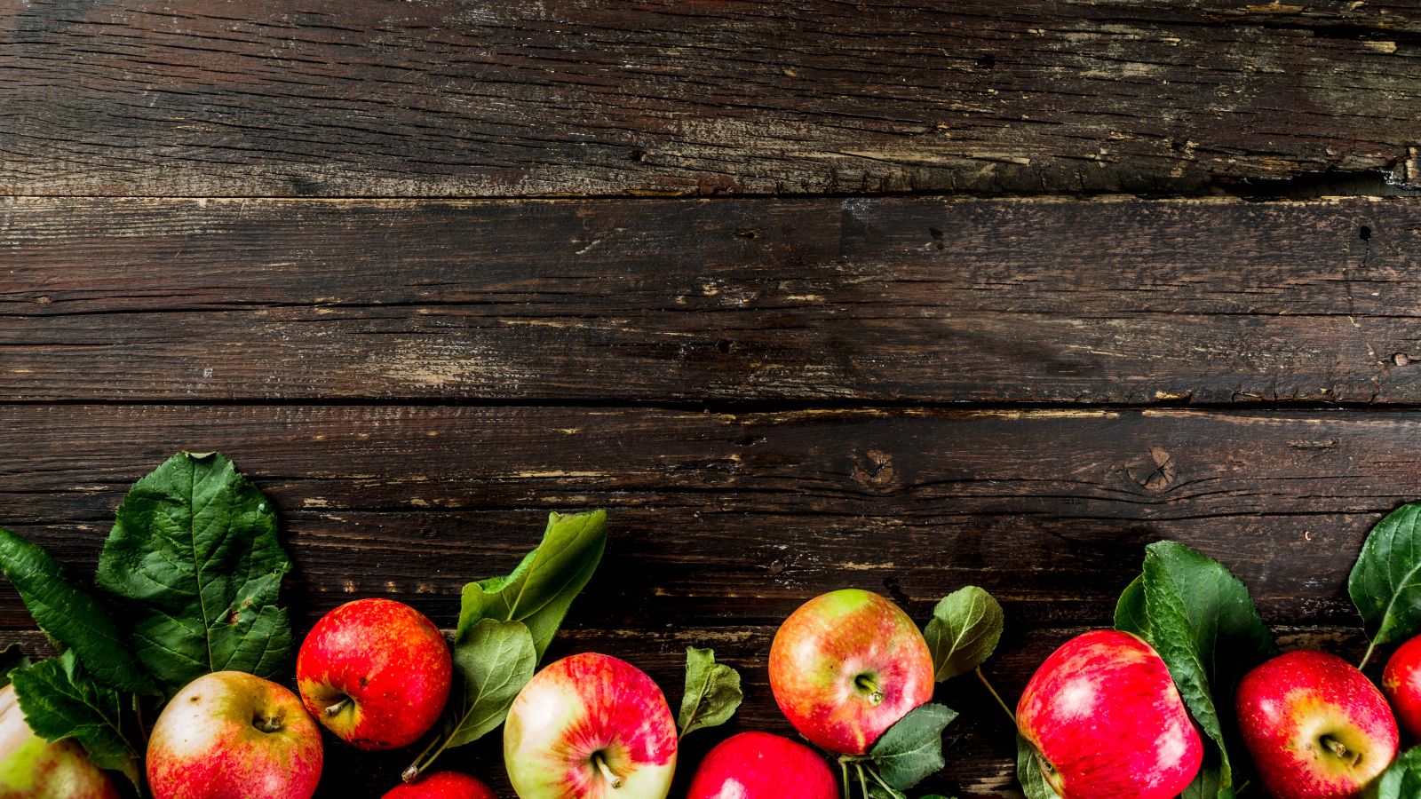 Fresh red apples with leaves on rustic wooden background