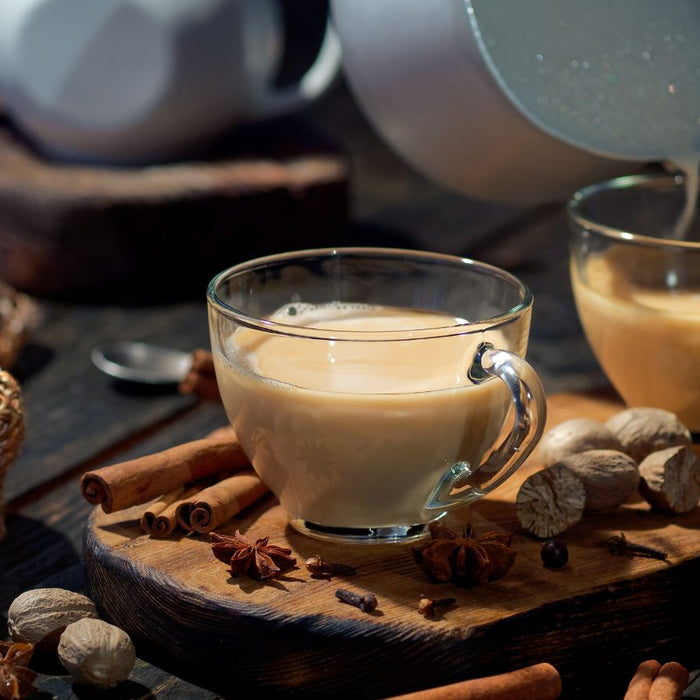 Two glass cups of chai tea with spices and a cozy setting