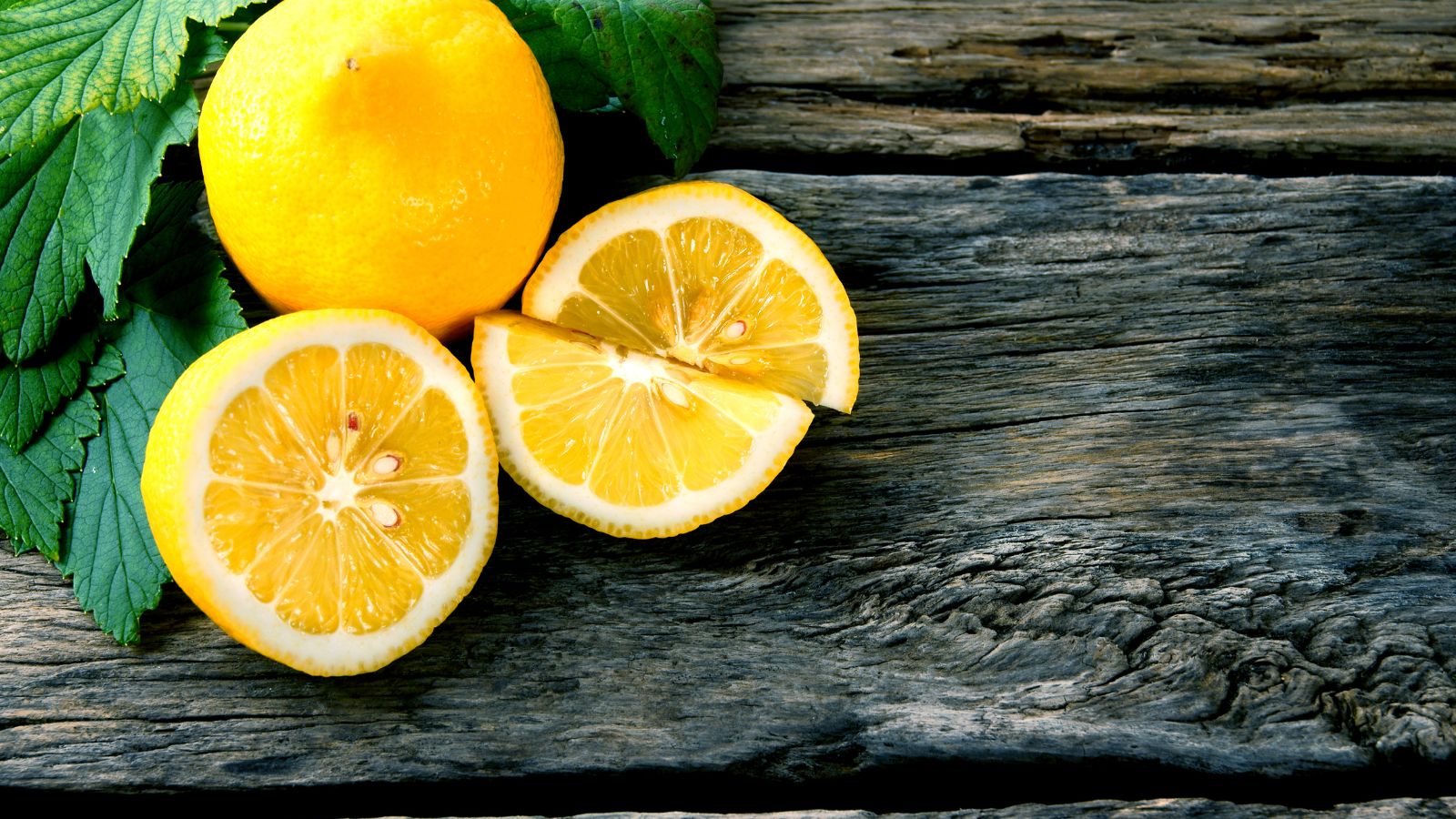 Sliced lemons with whole lemon and green leaves on old wooden surface