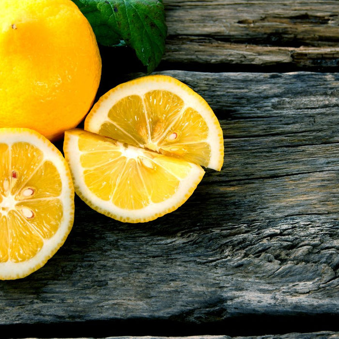 Sliced lemons with whole lemon and green leaves on old wooden surface