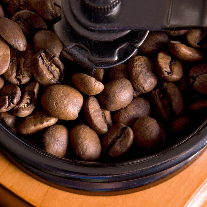 Top view of coffee beans in a manual grinder on a wooden surface.