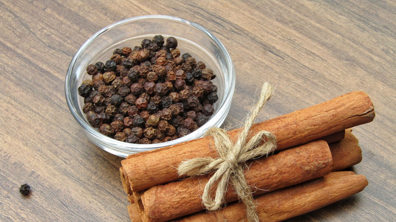 Cinnamon sticks tied with rope beside bowl of black pepper.