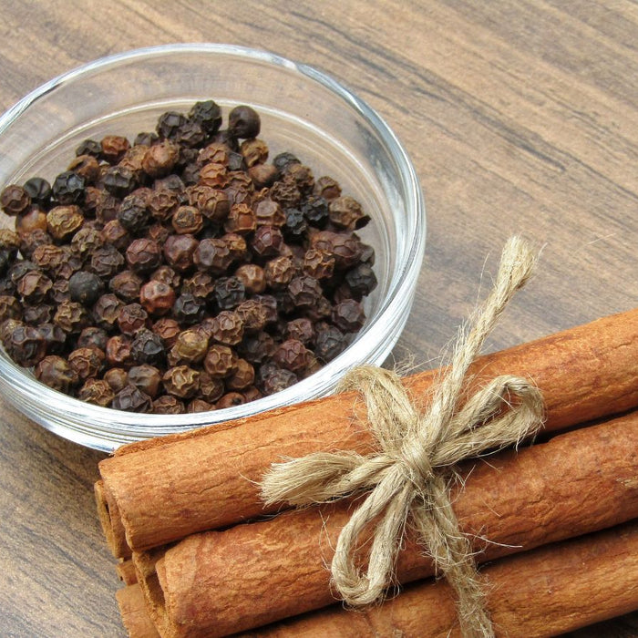 Cinnamon sticks tied with rope beside bowl of black pepper.