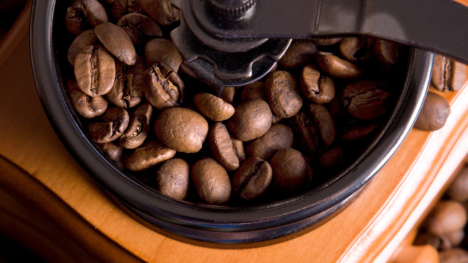 Top view of coffee beans in a manual grinder on a wooden surface.