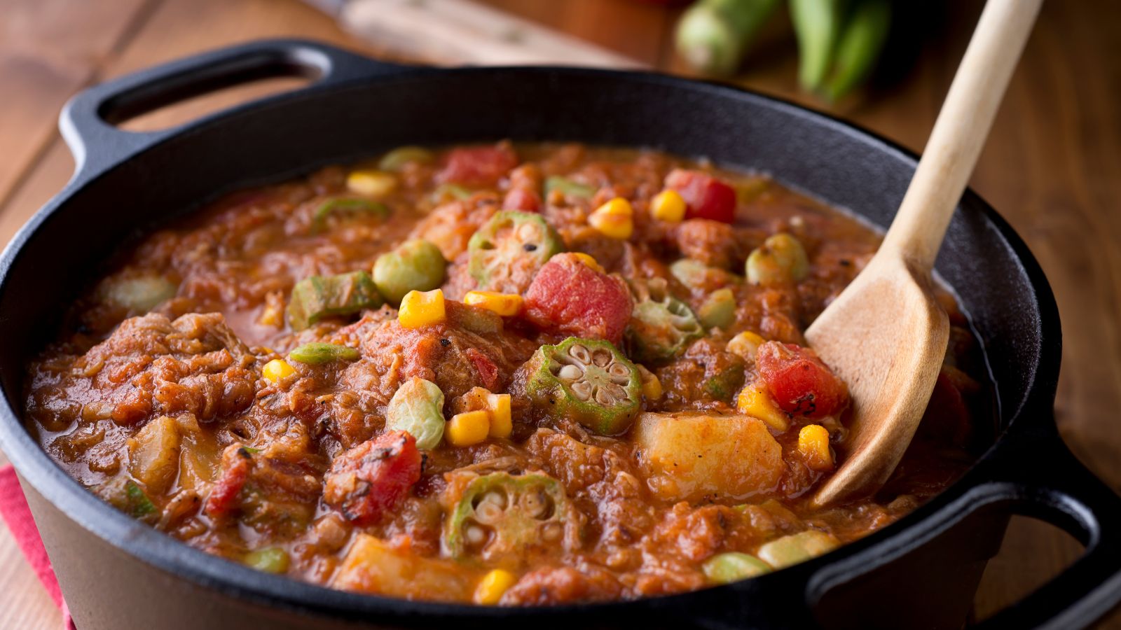 Beef stew with tomatoes, corn, and okra cooking in a black pot