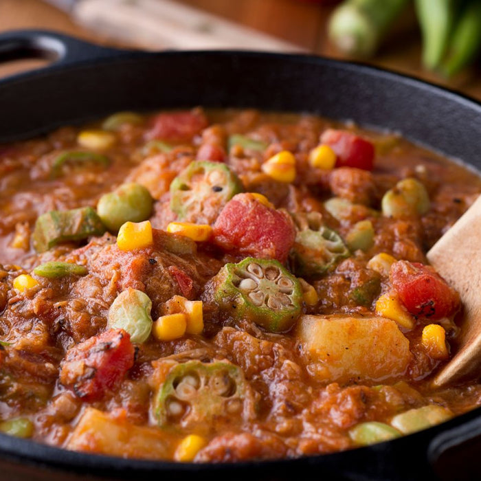Beef stew with tomatoes, corn, and okra cooking in a black pot