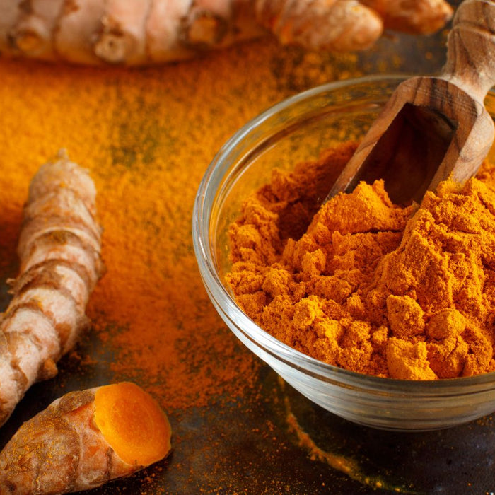 Bowl of turmeric powder with sliced roots on dark textured plate