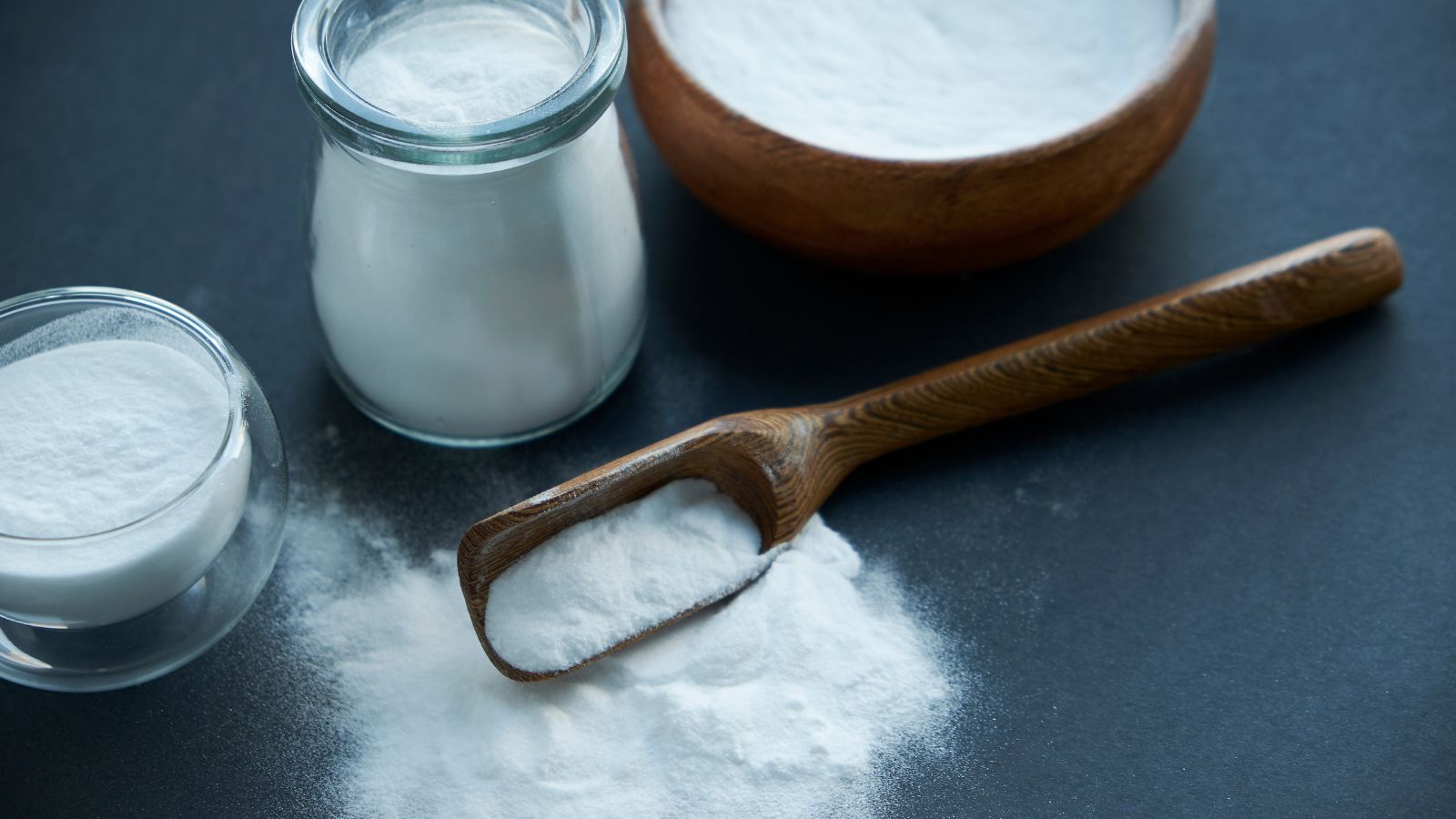 Baking soda in glass jars and wooden spoon on dark background.