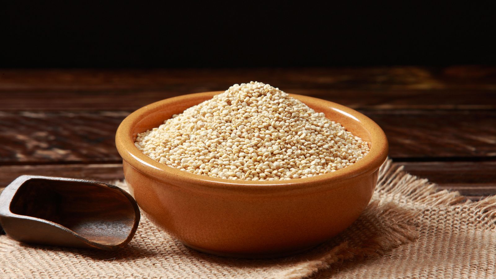 Bowl of dry white quinoa seeds on wooden table.
