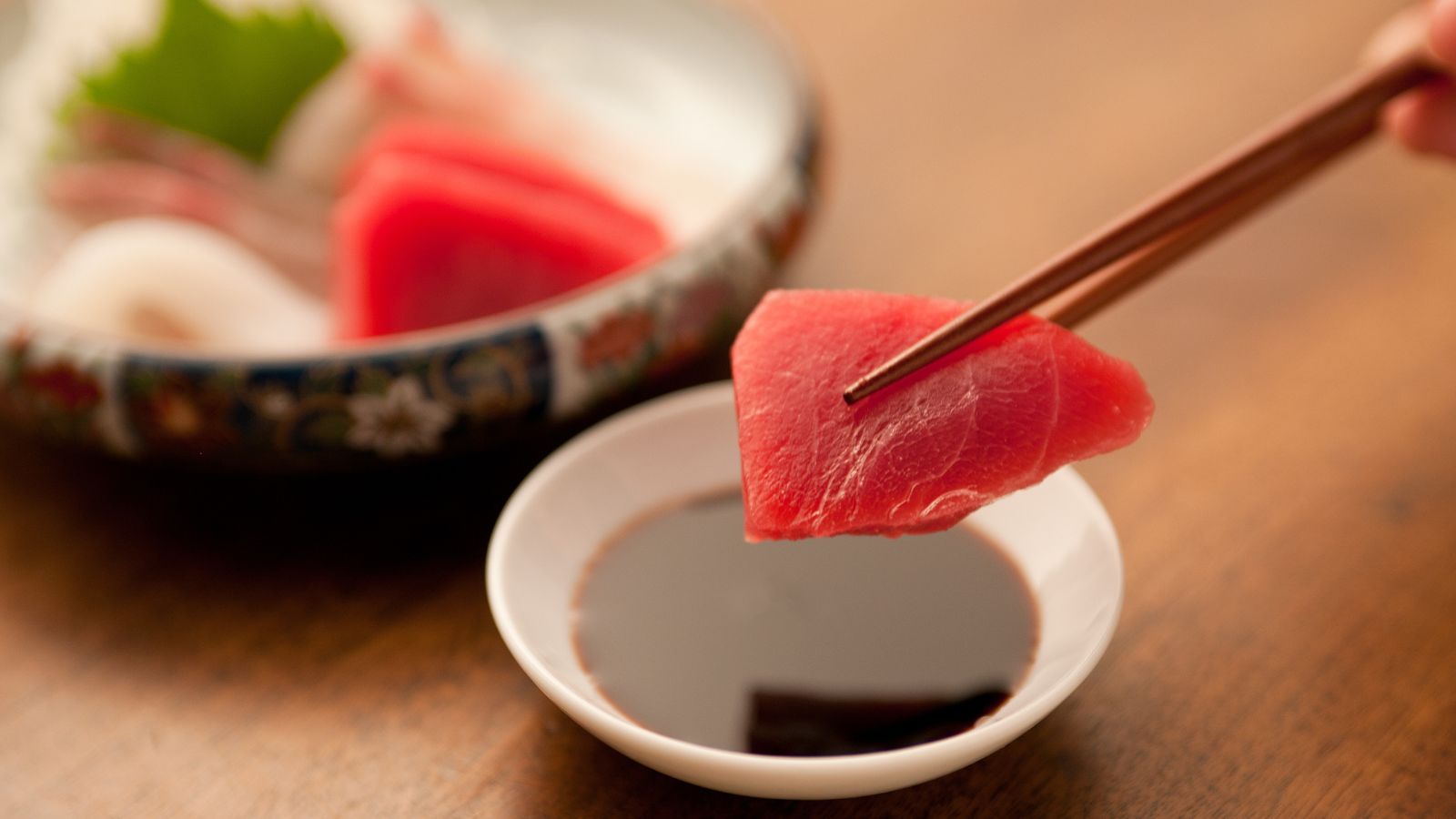 Piece of tuna sashimi dipped in soy sauce with chopsticks