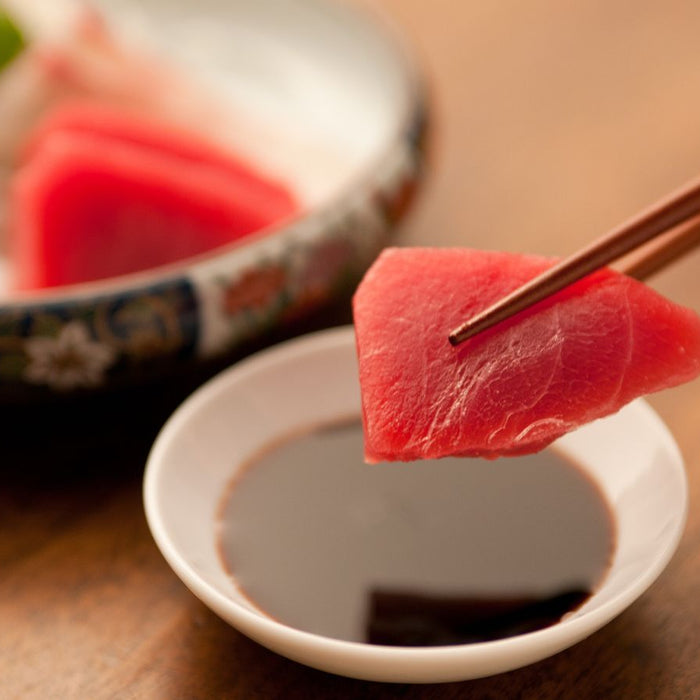 Piece of tuna sashimi dipped in soy sauce with chopsticks