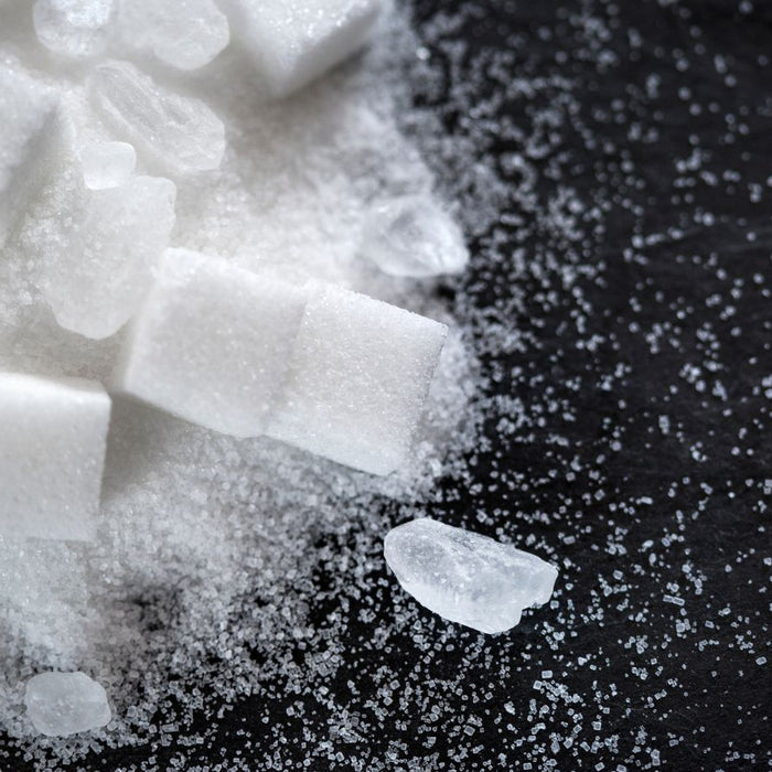 Close-up of sugar cubes and crystals scattered on black surface.
