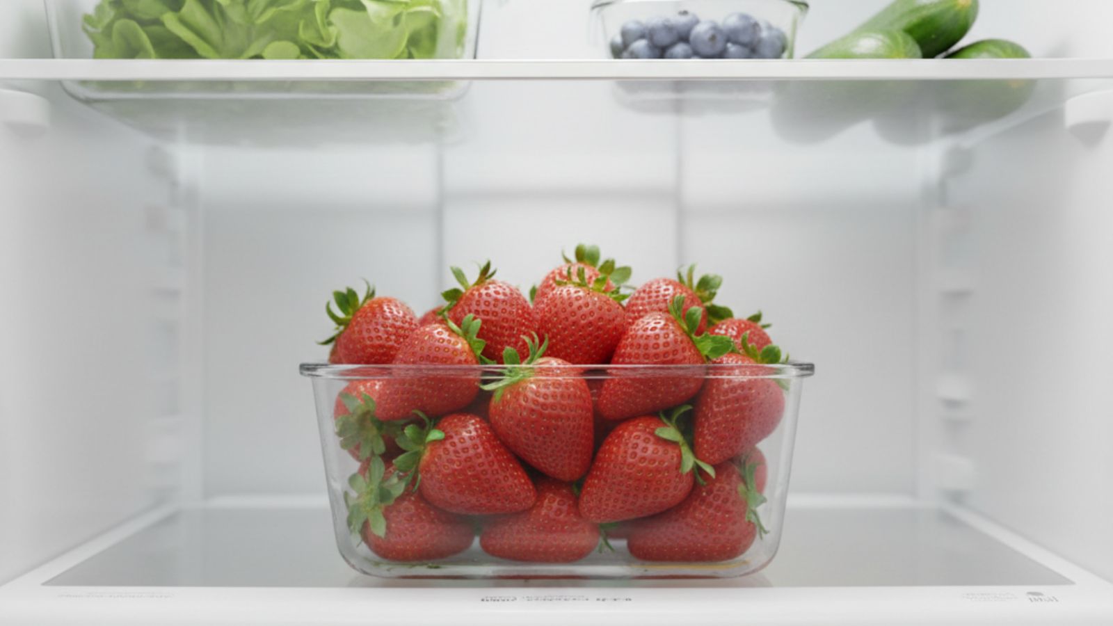 Glass container of fresh strawberries stored on a refrigerator shelf