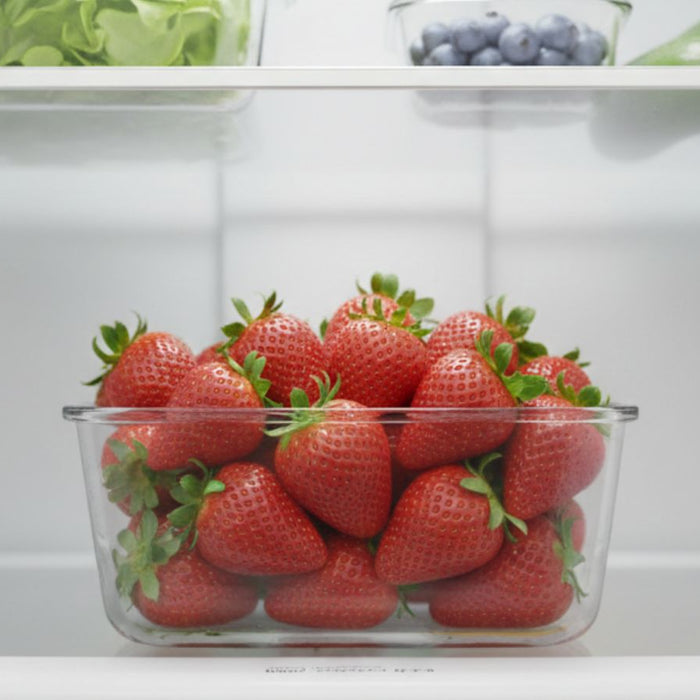 Glass container of fresh strawberries stored on a refrigerator shelf