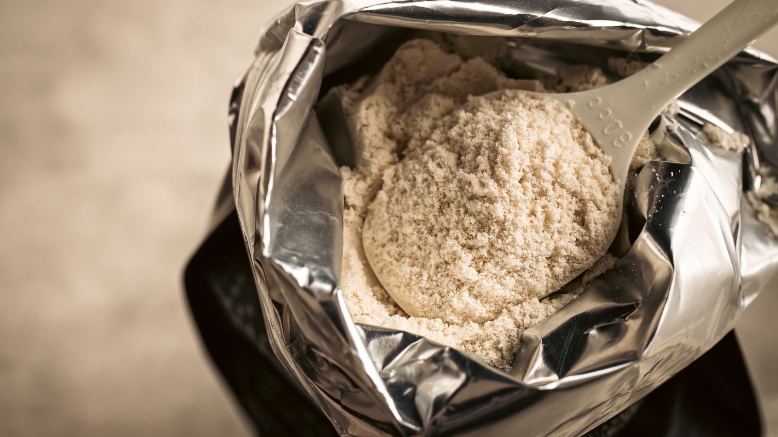 Open pouch of protein powder with scoop resting on top