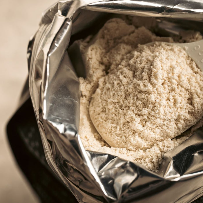 Open pouch of protein powder with scoop resting on top