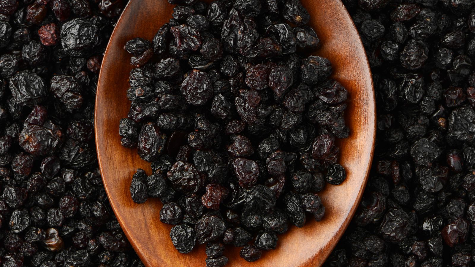 Wooden spoon filled with dried black currants on a black background.