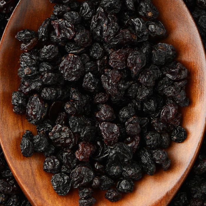 Wooden spoon filled with dried black currants on a black background.