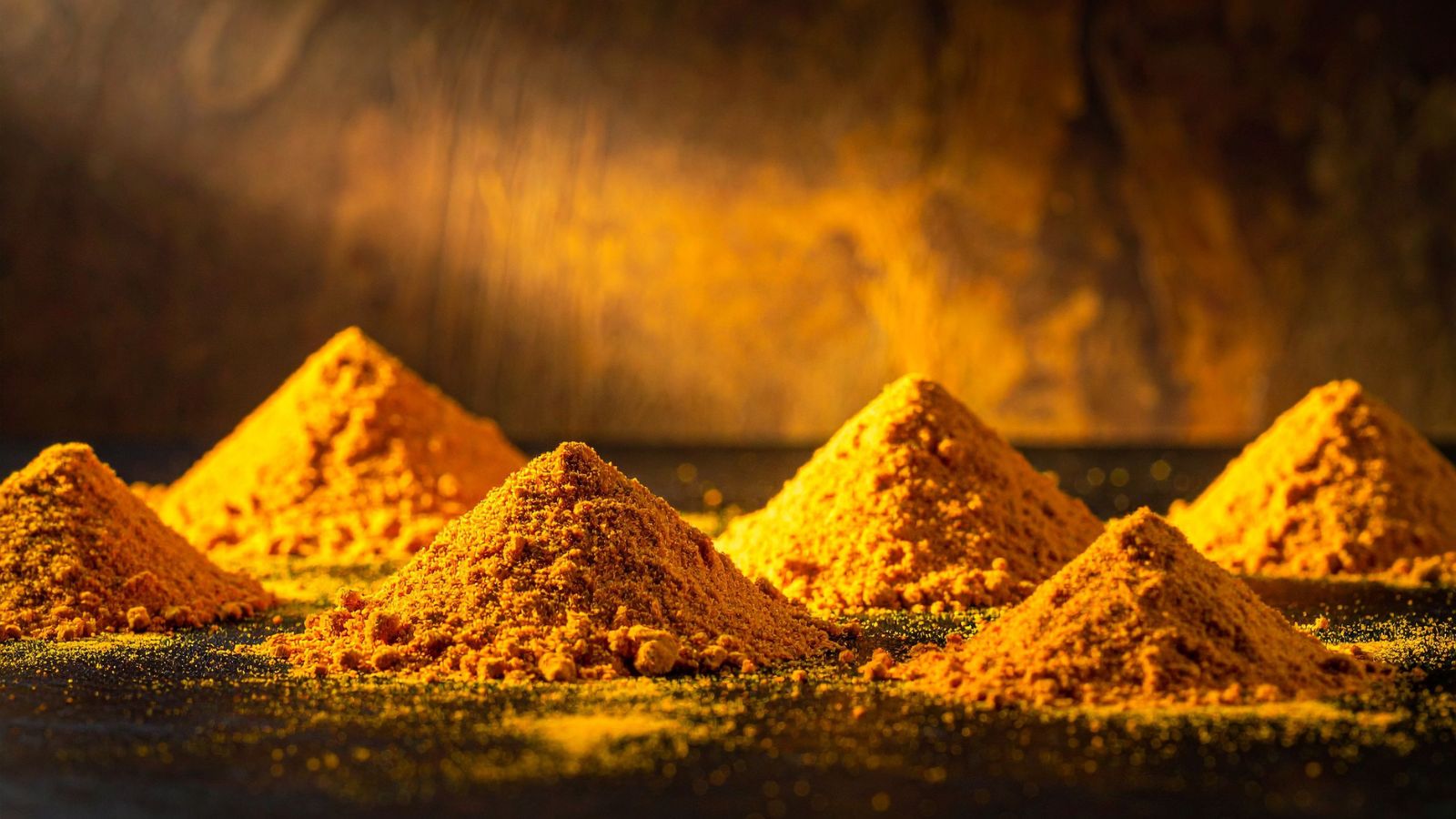 Mounds of golden turmeric powder arranged on dark surface