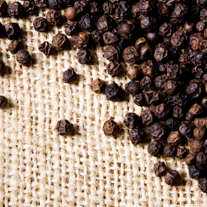 Black peppercorns scattered on burlap fabric texture