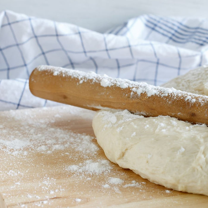 Dough with rolling pin on floured surface and kitchen towel.