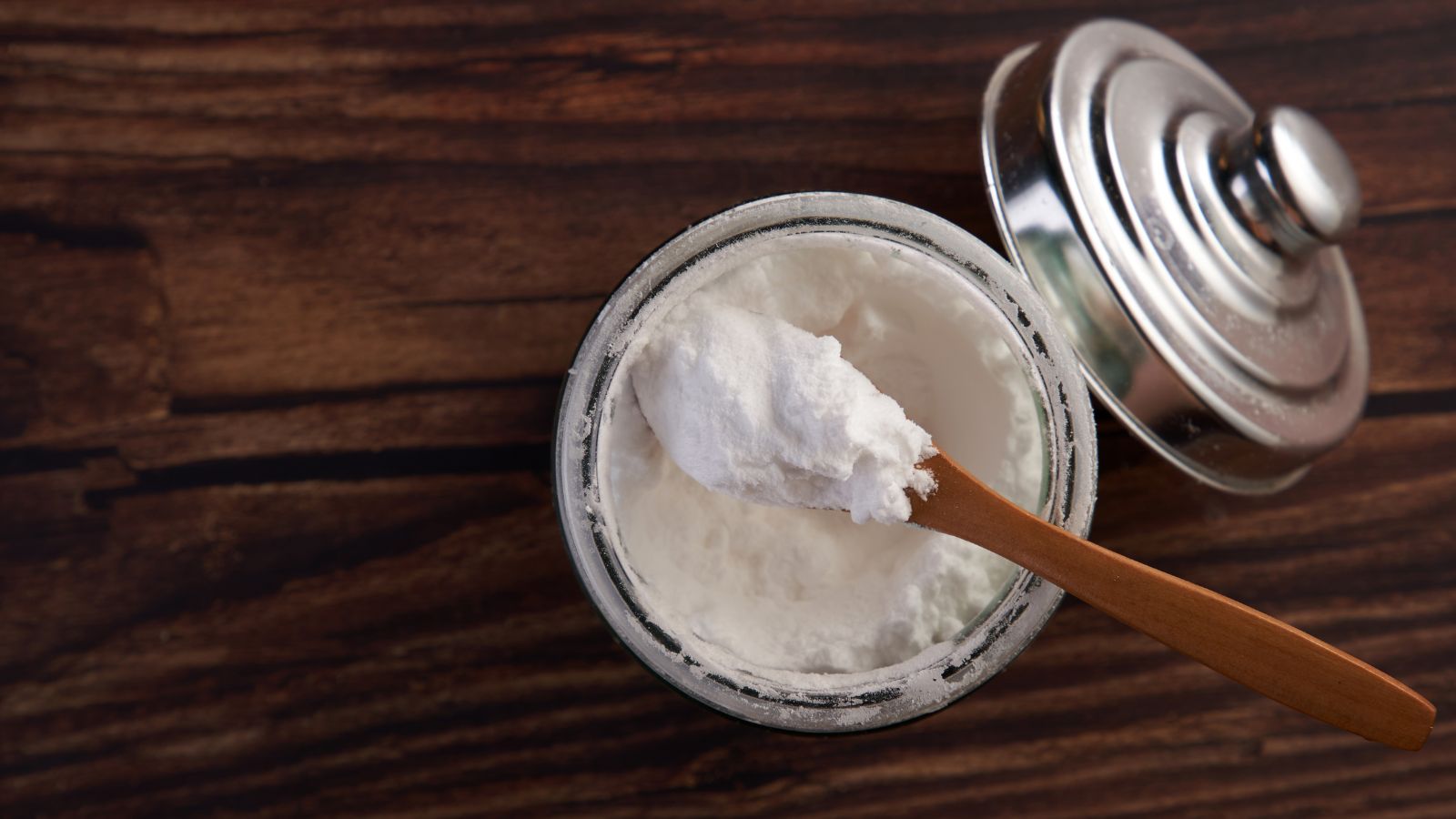 Glass jar of baking soda with wooden spoon on rustic wood table.