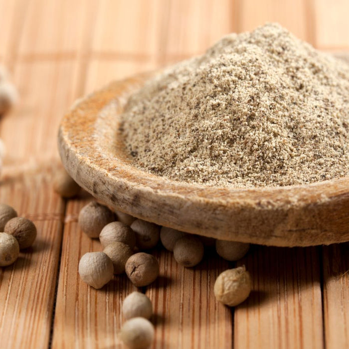Ground white pepper powder in wooden spoon with peppercorns.