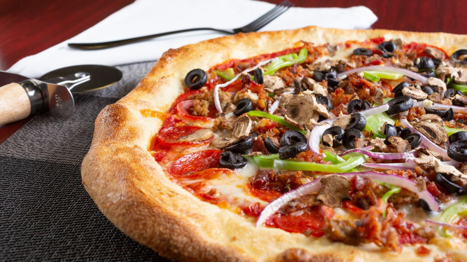 Close-up of loaded pizza with olives, mushrooms, and peppers.