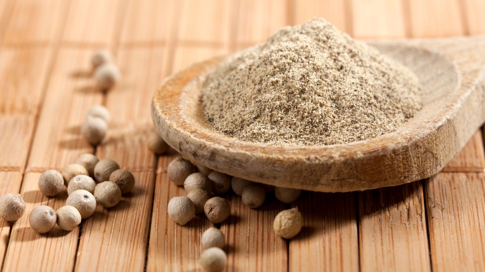 Ground white pepper powder in wooden spoon with peppercorns.