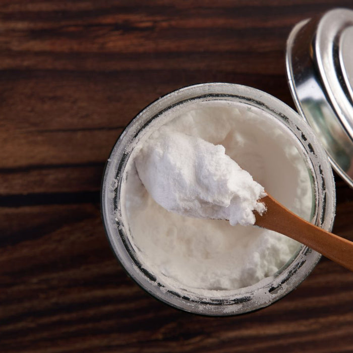 Glass jar of baking soda with wooden spoon on rustic wood table.