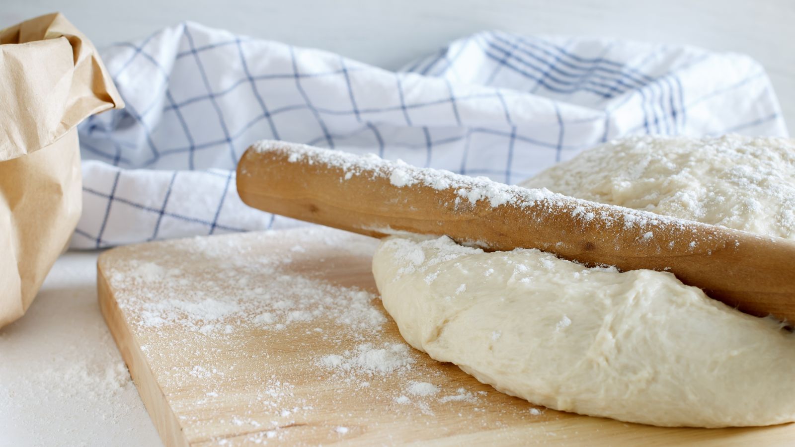 Dough with rolling pin on floured surface and kitchen towel.