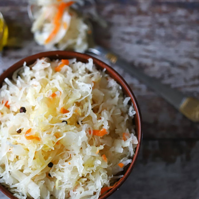 Bowl of sauerkraut with carrots and peppercorns on table.
