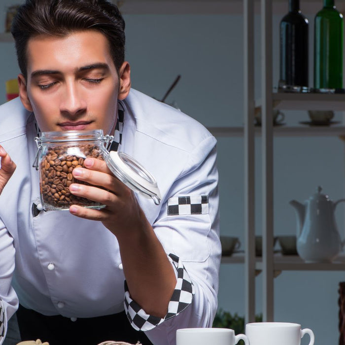 Barista smelling fresh coffee beans from a glass jar